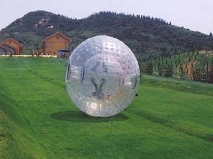 Giant inflatable Zorb ball rolling on a grassy hill, perfect for outdoor fun and events. Buy online in NZ for unique and thrilling entertainment.